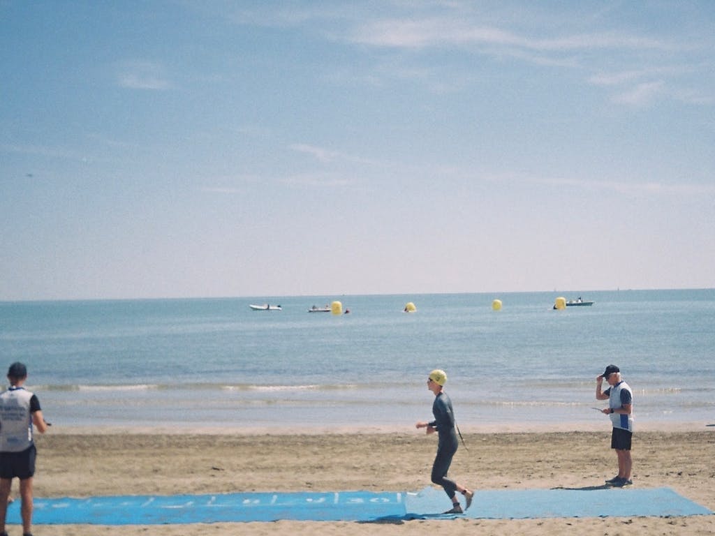 Athletes competing in beach triathlon with running and ocean backdrop.