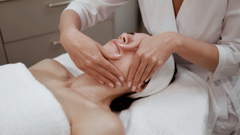 Practitioner's hands massaging the jaw and cheeks of a client lying on a towel-covered table